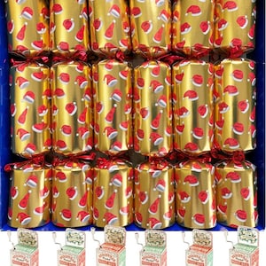 Peut inclure: Une boîte de crackers de Noël dorés avec des motifs de bonnets de Père Noël rouges. Chaque cracker est noué avec un ruban rouge. En dessous, plusieurs petites boîtes à musique décoratives avec le texte "Pocket Music Box" et "Jingle Bells".