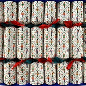 May include: A box of Christmas crackers, each wrapped in patterned paper featuring nutcracker figures in red, green, blue, and gold. The crackers are tied with red and green ribbons, arranged in a blue box.