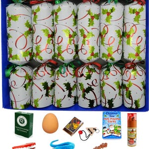 May include: A set of eighteen white Christmas crackers decorated with green holly leaves and red ribbons, arranged in a blue box. Below are various small toys including a green quiz box, a brown egg, a puzzle, playing cards, pencils, teeth, a blue worm, a whistle, and a snowman game.
