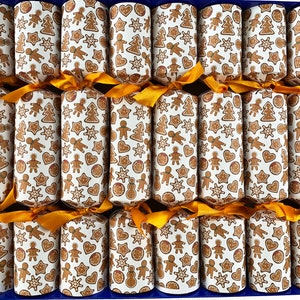 May include: A box of Christmas crackers with a blue base. Each cracker is wrapped in white paper with a repeating pattern of gingerbread cookies in various shapes. Gold ribbons secure the ends of each cracker, adding a festive touch.