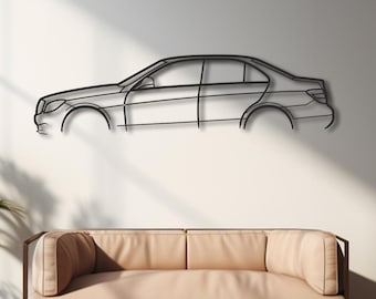 Puede incluir: Arte mural de contorno de coche de metal negro. La obra de arte está montada en una pared blanca sobre un sofá beige. La habitación tiene pisos de madera y plantas en macetas a ambos lados del sofá.