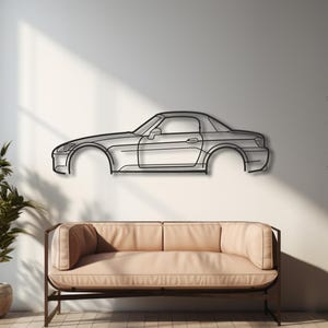 Könnte beinhalten: Ein minimalistisches Metall-Wandkunstwerk, das eine Autosilhouette darstellt. Das Kunstwerk ist an einer weißen Wand über einem beigen Sofa angebracht. Der Raum verfügt über Hartholzböden, Topfpflanzen und ein großes Fenster.