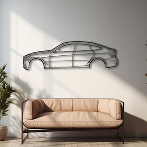 Puede incluir: Una pieza de arte mural de metal plateado que representa el perfil lateral de un coche. La obra de arte está montada en una pared blanca sobre un sofá marrón claro. La habitación es luminosa, con una gran ventana y plantas. El diseño del coche es minimalista.