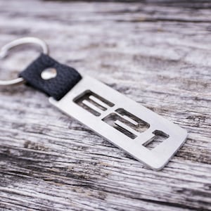 May include: A silver metal keychain with a black leather strap and the number "22" cut out of the metal.