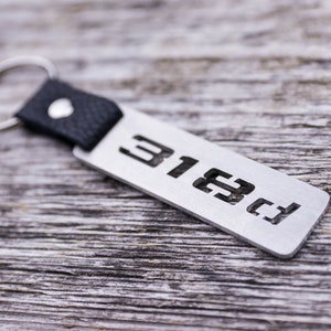 May include: A silver metal keychain with a black leather strap and a key ring. The keychain has the number "3182" engraved on it.