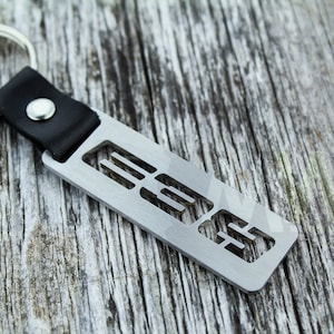 May include: A silver metal keychain with a black leather strap and a cutout design that reads "E33".