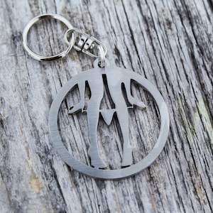 Può includere: Un portachiavi in metallo argentato con un design a taglio circolare di gambe di una persona. Il portachiavi è attaccato a un anello in metallo argentato.