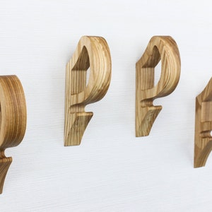 Op de afbeelding: Vier houten wandhaken in de vorm van de letter "P" gemonteerd op een witte muur. De haken zijn gemaakt van lichtbruin hout met een natuurlijke houtnerf.