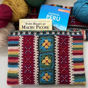 May include: A colorful crocheted pouch with a geometric pattern and beaded accents. The pouch is partially covered by a book titled "Essential Peru: Turn Right at Machu Picchu".