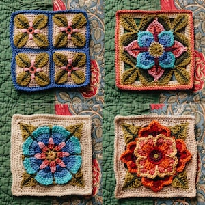 May include: Four crocheted squares with floral designs. The squares are in shades of green, blue, pink, orange, and brown. The squares are arranged in a grid pattern on a fabric background.