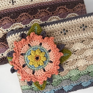 May include: Two crocheted bags with a floral design. The top bag is a multi-colored striped design with a scalloped edge. The bottom bag is a beige and brown design with a large crocheted flower in the center.