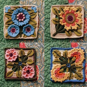 Op de afbeelding: Vier gehaakte vierkanten met bloemmotieven. Elk vierkant heeft een ander bloemmotief in tinten groen, blauw, geel en rood.