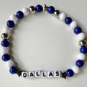 May include: A blue and white beaded bracelet with silver stars and letter beads spelling "DALLAS".