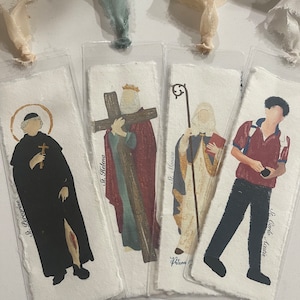 Może przedstawiać: Cztery zakładki z r&oacute;żnymi postaciami religijnymi i jedną osobą. Zakładki są wykonane z papieru i mają białe tło. Postacie są namalowane w realistycznym stylu. Zakładki mają r&oacute;żne rozmiary i kształty. Tekst na zakładkach brzmi: "St. Perccrine", "St. Helena", "St. Monica" i "St. Carlo Acutis".