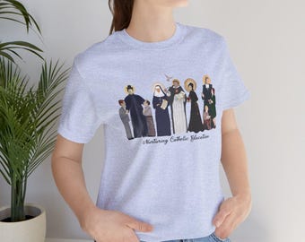 Op de afbeelding: Een heidekleurig T-shirt met een afbeelding van een groep mensen in religieuze kleding. De tekst "Nurturing Catholic Education" is onder de afbeelding gedrukt.