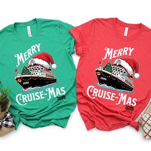 May include: Two short-sleeved t-shirts, one green and one red, feature a Christmas cruise ship graphic. The graphic includes a ship with a Santa hat, the words "Merry Cruise-Mas 2025", and the name "Emma".