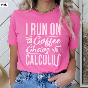 May include: Pink t-shirt with the text "I run on coffee, chaos, and calculus" in white. The shirt features a small graphic of a coffee cup with an infinity symbol.