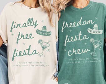 May include: Two t-shirts, one ivory and one light green, with the words "finally free fiesta" and "freedom fiesta crew" in a script font. Each shirt has a sombrero and a cocktail graphic. The text "Olivia's Fresh Start Party, June 8, 2026 - San Antonio, TX" is also printed.