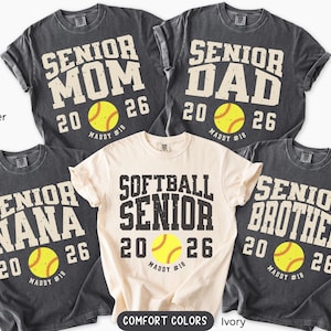 May include: Five t-shirts with softball-themed designs. The shirts are in various colors, including pepper and ivory. Each shirt features the words "Senior Mom," "Senior Dad," "Senior Nana," "Softball Senior," and "Senior Brother," along with the year "2026" and a softball graphic.