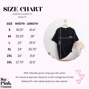 May include: Black t-shirt hanging on a wooden hanger, with a size chart. The chart lists sizes S to 3XL, with width and length measurements in inches. The text reads "SIZE CHART" and "Unisex fit". The shirt is made of 100% ethically grown ring-spun US cotton.
