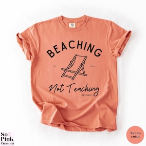 Comfort Colors Shirt with deck chair illustration in the center, curved text above, script below - BEACHING Not Teaching #Retired Year Est. 2026