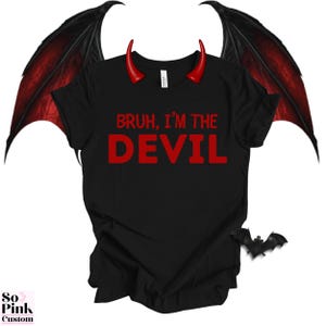 May include: Black t-shirt with the red text "BRUH, I'M THE DEVIL." The shirt is adorned with red devil horns and black and red wings. A small bat silhouette is also present. The shirt is part of a costume or novelty apparel collection.