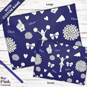 May include: Two navy blue zippered pouches, one large and one small, with a white cheerleader-themed pattern. The pattern includes pom-poms, megaphones, bows, hearts, and the name "Olivia". The text "WITH CUSTOM NAME" is visible.