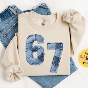 May include: A sand-colored sweatshirt with the number "67" in a faux denim patchwork design. The sweatshirt is laid on top of a pair of blue jeans. The words "Faux Patchwork Print" are on a yellow starburst.
