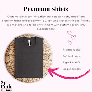 May include: A dark gray t-shirt on a woven straw mat. The t-shirt is made from soft, eco-friendly fabric and is available in custom designs. The text "So Pink Custom" is in the lower left corner of the image.