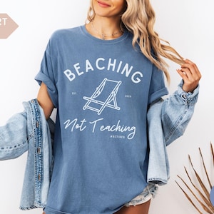Comfort Colors Shirt with deck chair illustration in the center, curved text above, script below - BEACHING Not Teaching #Retired Year Est. 2026