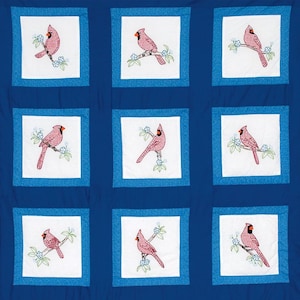 Puede incluir: Una colcha azul con fondo blanco que presenta nueve cuadrados con cardenales rojos bordados en ramas con flores blancas. Cada cuadrado tiene un borde azul.
