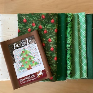 May include: A collection of folded fabric pieces in various shades of green, red, and white, featuring patterns of pine branches, red ornaments, candy canes, and gold stars. A brown paper pattern packet labeled Fa La La Running Doe Quilts is included.
