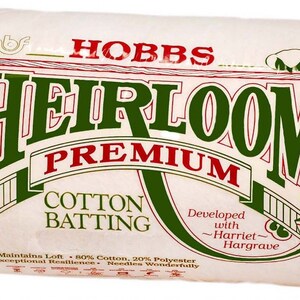 May include: A package of Hobbs Heirloom Premium Cotton Batting. The white batting is wrapped in clear plastic. The label features green and red text that reads "Heirloom Premium Cotton Batting". The package also states "Maintains Loft, 80% Cotton, 20% Polyester".