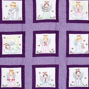 Puede incluir: Una colcha acolchada con un borde de patrón floral púrpura y una cuadrícula de cuadrados de ángeles bordados. Cada cuadrado presenta un diseño de ángel diferente con halos, alas y varios objetos. Los ángeles son blancos, con acentos de rojo, verde y azul.