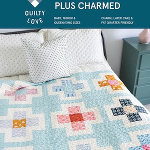 May include: A quilt pattern called "Plus Charmed" by Emily Dennis. The quilt is made with a blue background and features a pattern of white crosses with colorful fabric squares in the center. The quilt is displayed on a bed with white bedding and a white pillow with black polka dots.