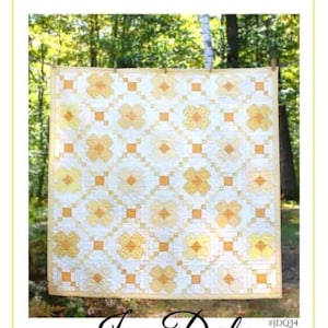 May include: A handmade quilt with a floral pattern in shades of yellow and white, hanging outdoors. The quilt features a repeating design of stylized flowers and square accents. The text "BUTTERCUP" and "Jen Daly Quilts" are visible.