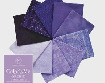 May include: A bundle of ten fat quarter fabric pieces arranged in a circular fan pattern, featuring various shades of purple, lavender, and deep violet. Some fabrics have textured patterns and gold accents. Includes a label reading Color Me ORCHID.