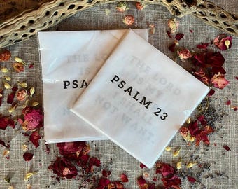 Könnte beinhalten: Zwei weiße, quadratische Taschentücher mit dem Text "PSALM 23" in Schwarz gedruckt. Der Satz "THE LORD IS MY SHEPHERD; I SHALL NOT WANT" ist ebenfalls auf den Taschentüchern aufgedruckt. Die Taschentücher sind von getrockneten Rosenblättern und anderen Pflanzen umgeben.