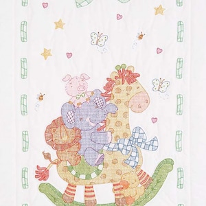 May include: A white quilted baby blanket with a green and white checkered bow in the top corner. The center of the blanket features a colorful embroidered scene of a giraffe, elephant, pig, and lion on a rocking horse. The scene is surrounded by small embroidered hearts, stars, butterflies, and bees.