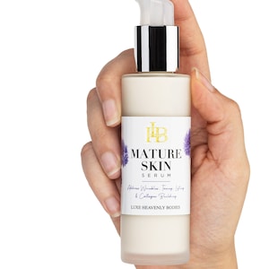 May include: A white bottle with a pump dispenser containing Mature Skin Serum. The bottle has a label with the text "Mature Skin Serum" and "Address Wrinkles, Firming, Lift & Collagen Building". The label also includes the text "Luxe Heavenly Bodies".