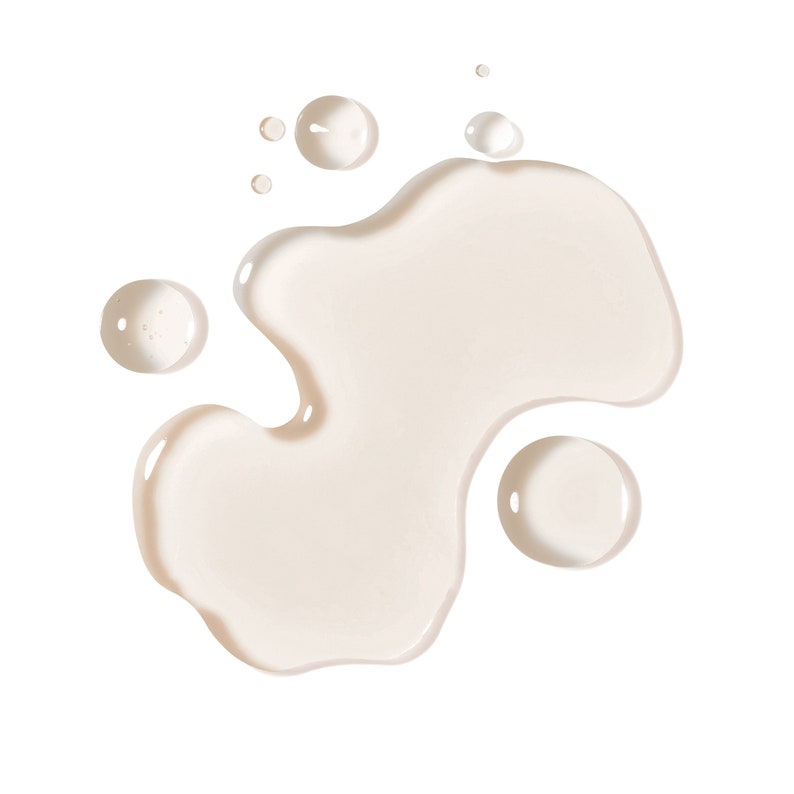 May include: A close-up shot of a light beige liquid, possibly a cosmetic product, spilled on a white background. The liquid forms an irregular shape with several smaller, round droplets scattered around it. The overall effect is clean and minimalist.