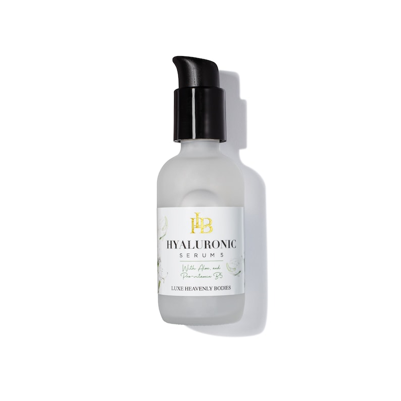 May include: A clear glass bottle with a black pump top dispenser. The bottle is labeled "HYALURONIC SERUM 5" with the text "With Aloe and Provitamin B5" and "LUXE HEAVENLY BODIES".