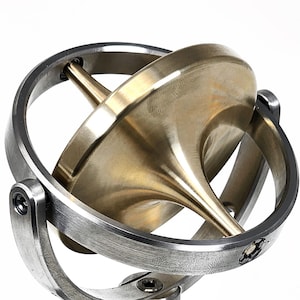 Peut inclure: Un gyroscope en métal composé d'une toupie en laiton poli suspendue dans un cadre à cardan en argent brossé. L'ensemble est monté sur une base circulaire en métal argenté à fond plat avec un support vertical central.