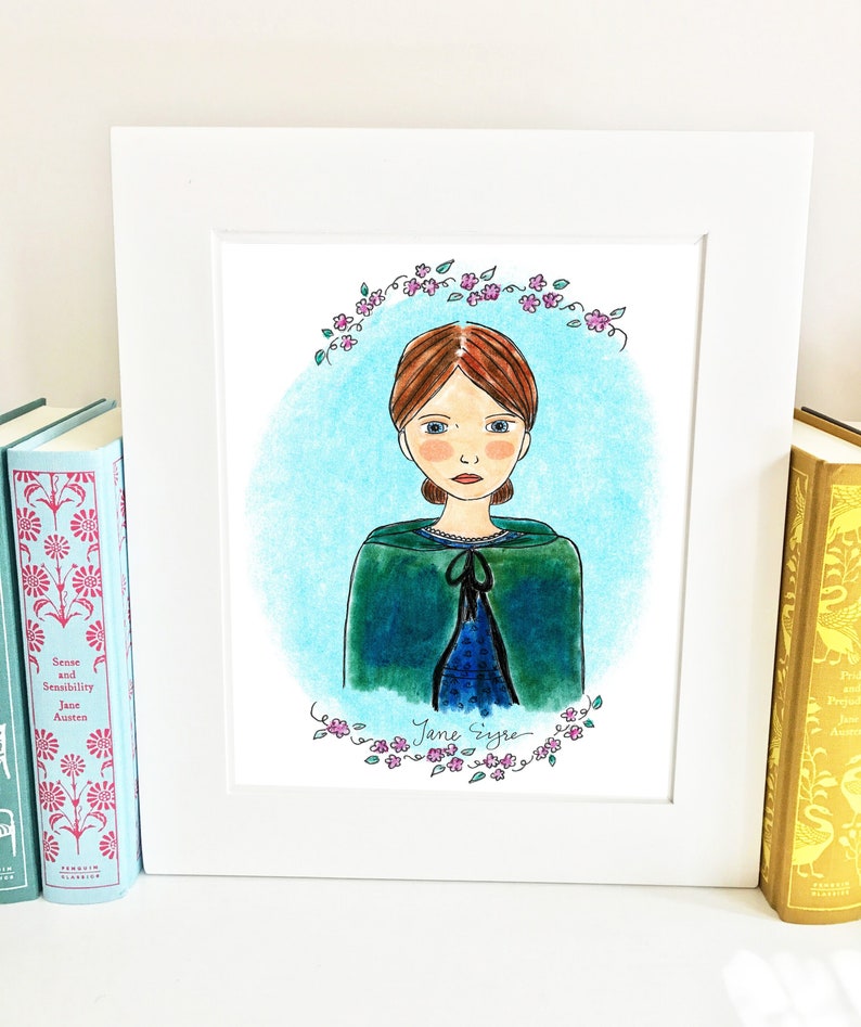 K&ouml;nnte beinhalten: Eine gerahmte Illustration von Jane Eyre, einer fiktiven Figur aus dem gleichnamigen Roman. Die Illustration ist in Aquarell ausgef&uuml;hrt und zeigt Jane Eyre in einem gr&uuml;nen Umhang mit einem blauen Kleid darunter. Die Illustration ist von einem Kranz aus rosa Bl&uuml;ten umgeben.