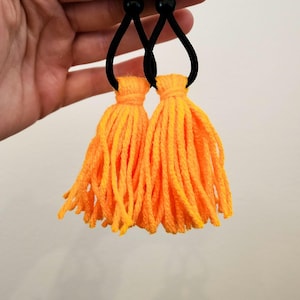 May include: Two orange tassel hair ties with black elastic bands.