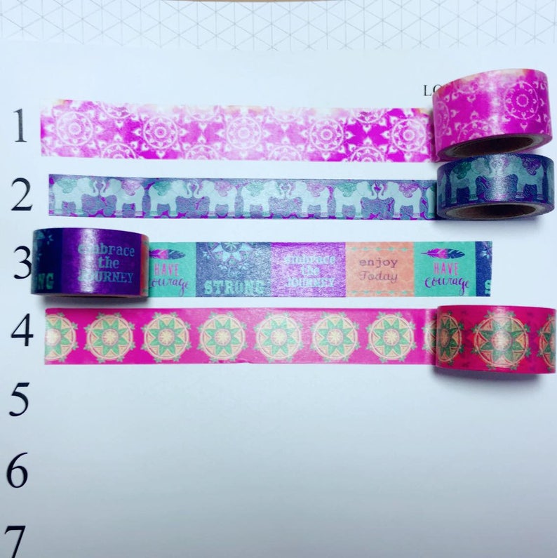 May include: Five rolls of washi tape with different designs. The first roll has a pink and white mandala pattern. The second roll has a purple and white elephant pattern. The third roll has a teal, pink, and purple pattern with the words "Embrace the Journey", "Have Courage", "Strong", "Embrace the Journey", and "Enjoy Today". The fourth roll has a pink and green mandala pattern. The fifth roll has a pink and red mandala pattern.