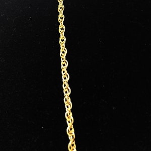 May include: A gold chain necklace with a delicate, linked design. The chain is shown against a black background.