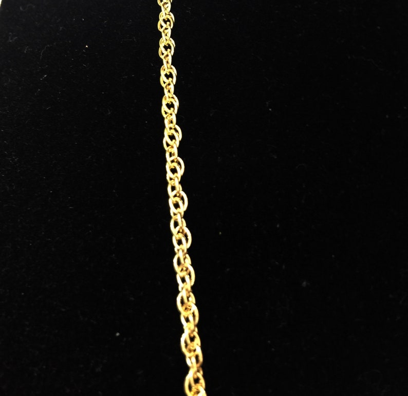 May include: A gold chain necklace with a delicate, linked design. The chain is shown against a black background.
