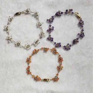 May include: Three delicate gold bracelets with gemstone accents. The bracelets feature clusters of small white, purple, and orange gemstones.