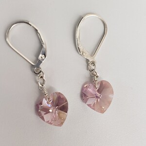 May include: A pair of silver dangle earrings with a light purple heart-shaped crystal charm.